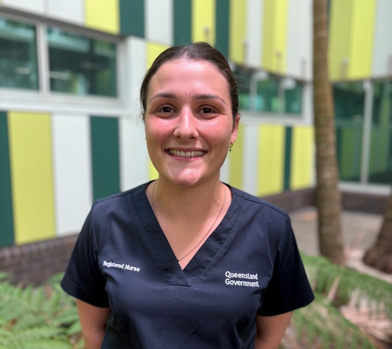 A nurse in scrubs smiles in a courtyard