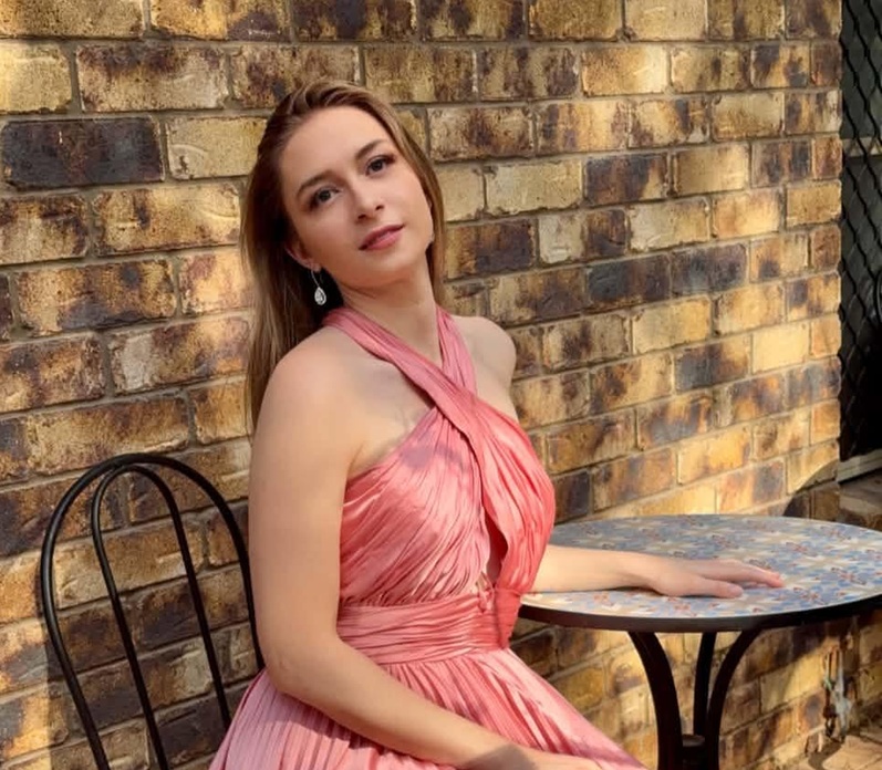 A young and pretty female doctor poses in an apricot formal dress while seated 
