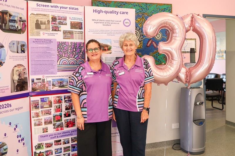 Two radiologists stand in front of a 30-year display for BreastScreen