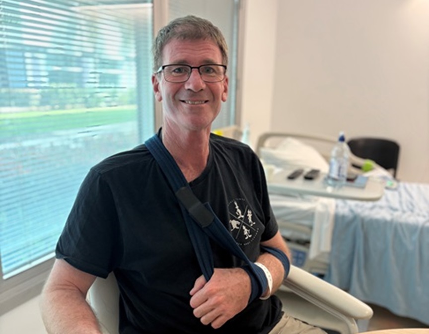 Man sits in chair with arm in a sling in hospital room
