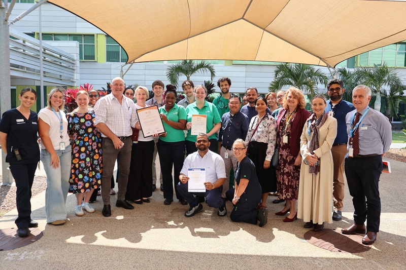 Group of staff hold accreditation certificates in the courtyard
