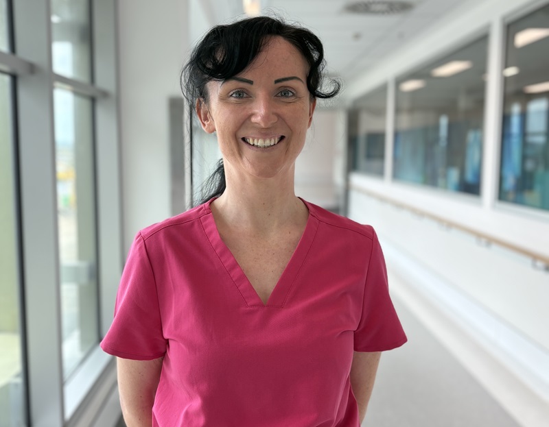 A nurse in pink scrubs stands in a hallway