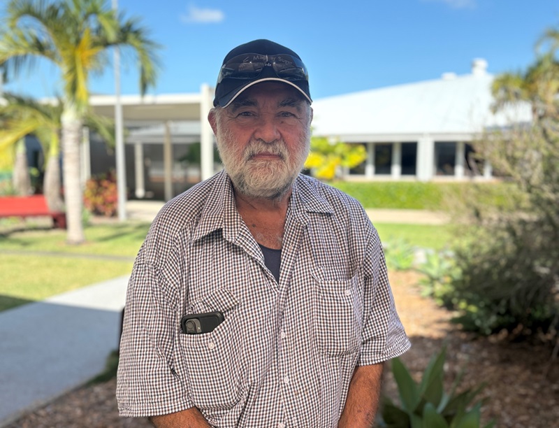 An man in his 60s with a beard stands in the courtyard of a hospital