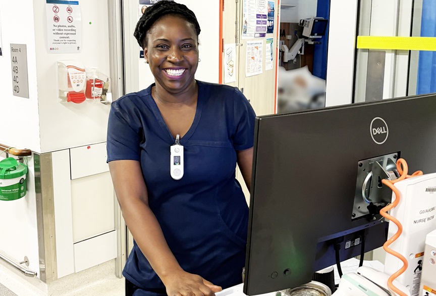 A dark skinner nurse stands in front of a computer in the stroke unit