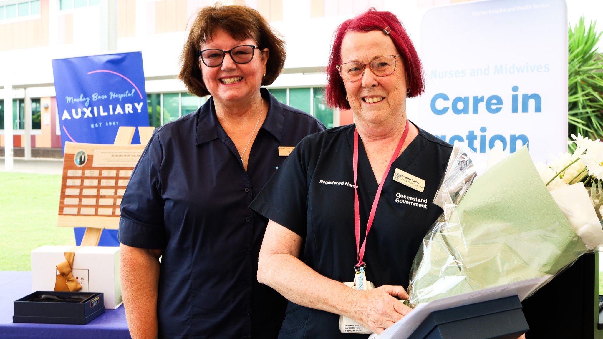 Two nurses pose with flowers and awards