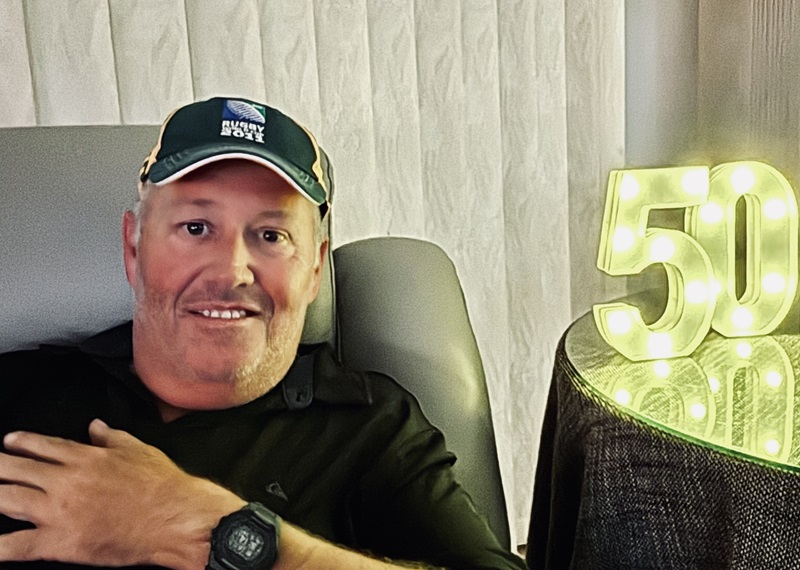 A man wearing a hat sits next to an illuminated 50 sign
