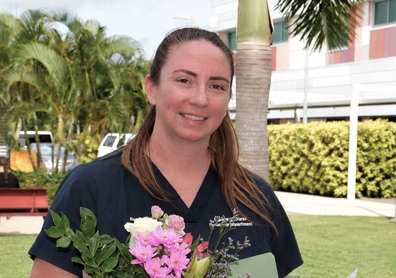 An award-winning nurse stands with flowers and a trophy