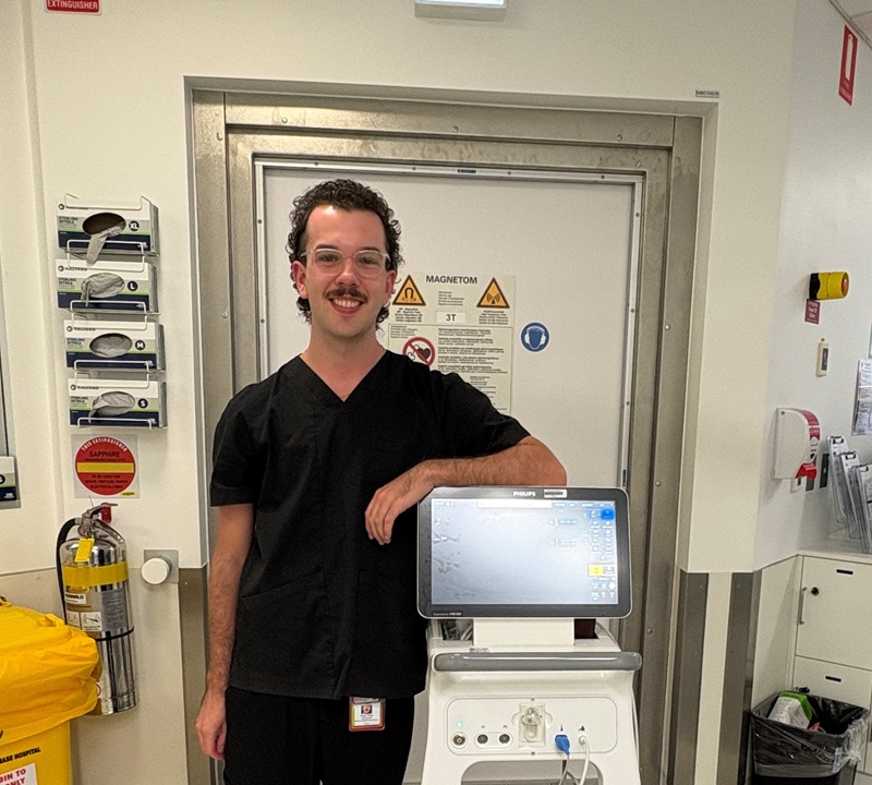 A radiologists stands with equipment in front of an MRI booth