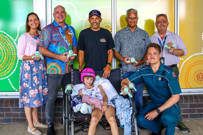 A group stands with a dad and daughter in a wheelchair with toy turtles
