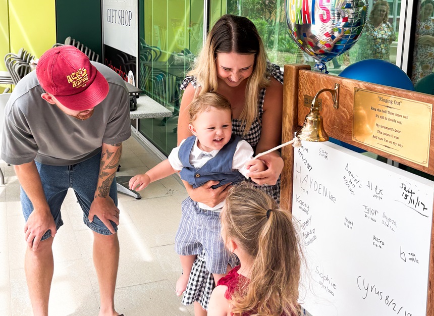 A toddler rings the bell with his mum, dad and little sister in the Mackay Base Hospital courtyard.