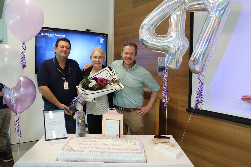 A veteran nurse stands with flowers, a cake and balloons