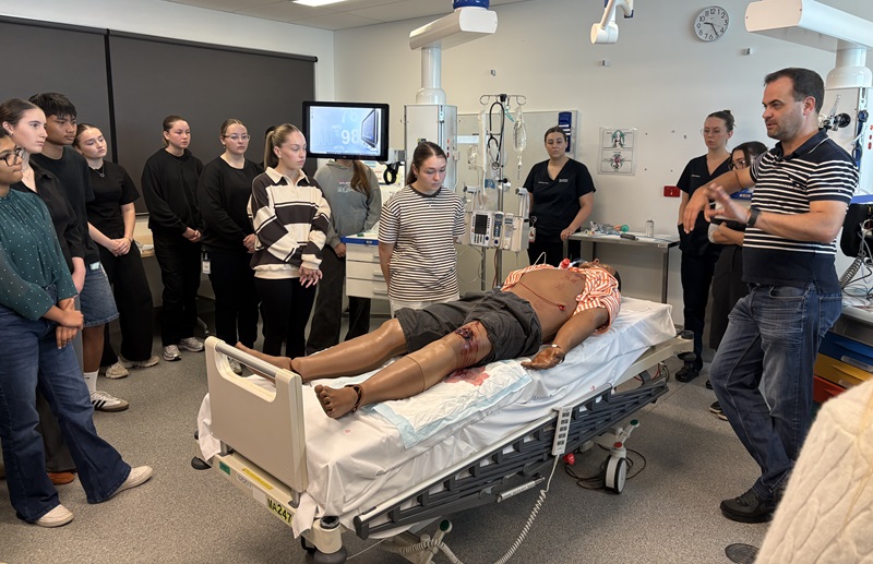 Students stand around a mannequin in an ED as a doctor speaks