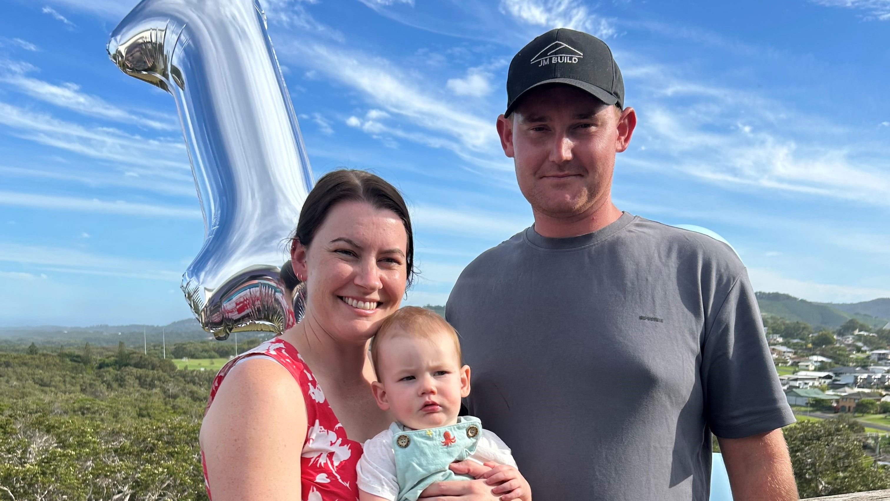 A mum and dad hold 1 year old son with balloon