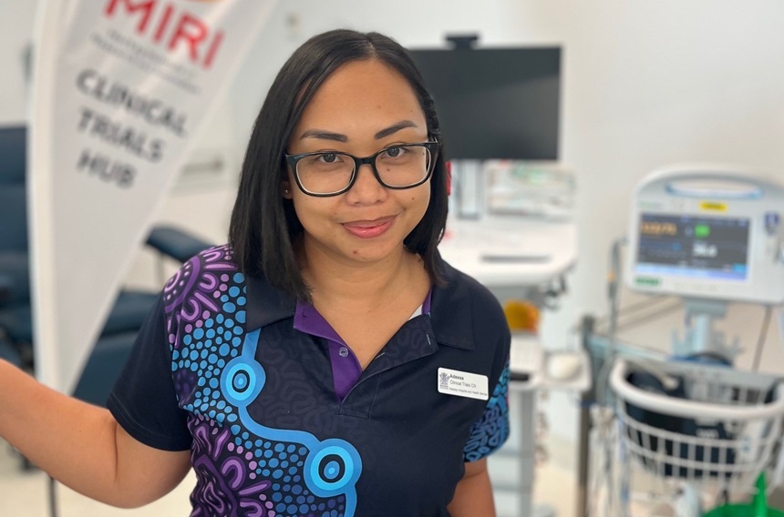 A clinical trials nurse poses in front of a MIRI banner